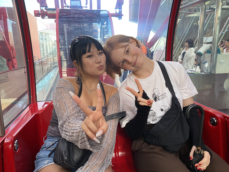 Two CET Japan housemates holding up peace signs while inside a red Hep Five Ferris Wheel cart in Osaka, Japan