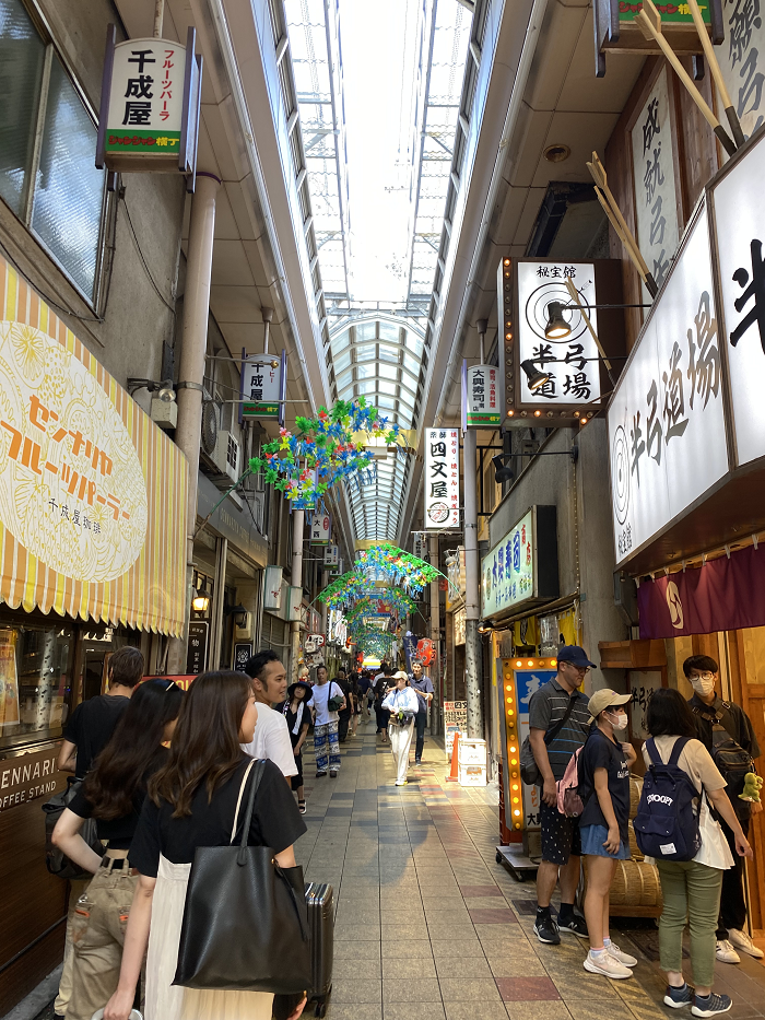 People lined up on either side of an indoor market around Tsutenkaku Tower in Japan