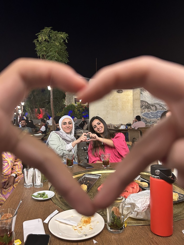 A heart formed by hands and inside are CET Jordan teachers sitting at a table for a farewell dinner with students 