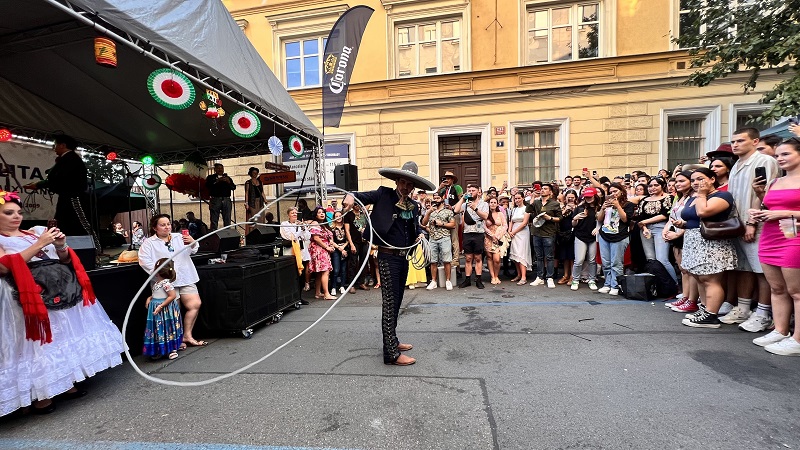 A male performing a Mexican lasso rope dance at a Mexican street festival in Prague with many people in the background filming the performance 