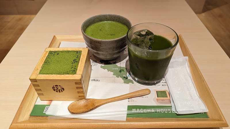 A Matcha cheesecake and Matcha drink on a wooden try with a wooden spoon