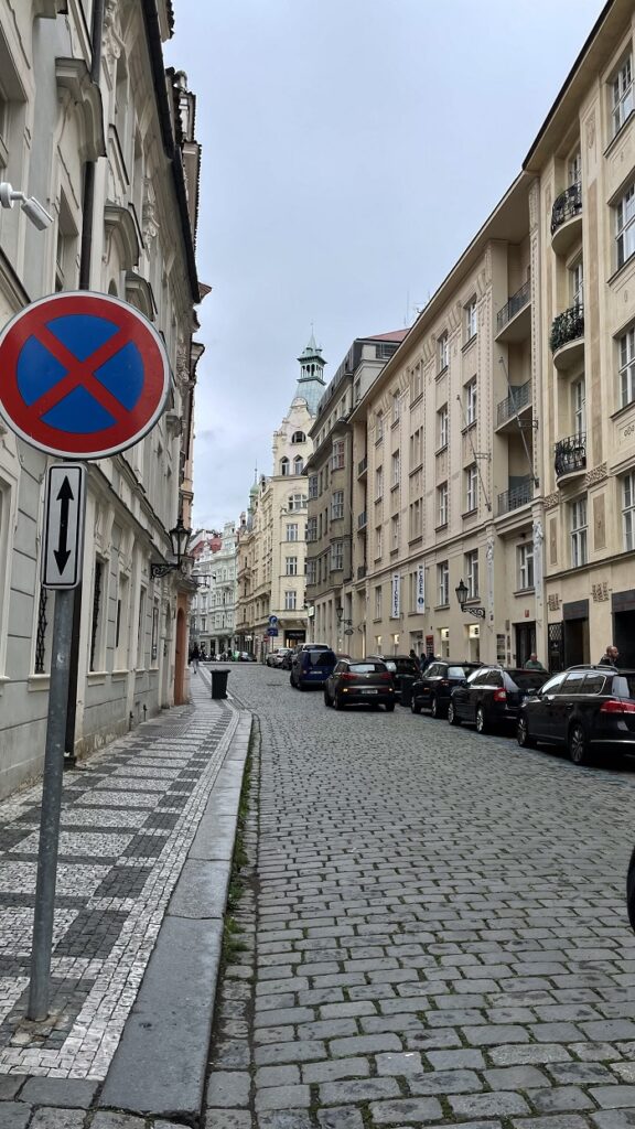 A narrow cobble-stoned street with cars in Prague on a gloomy day