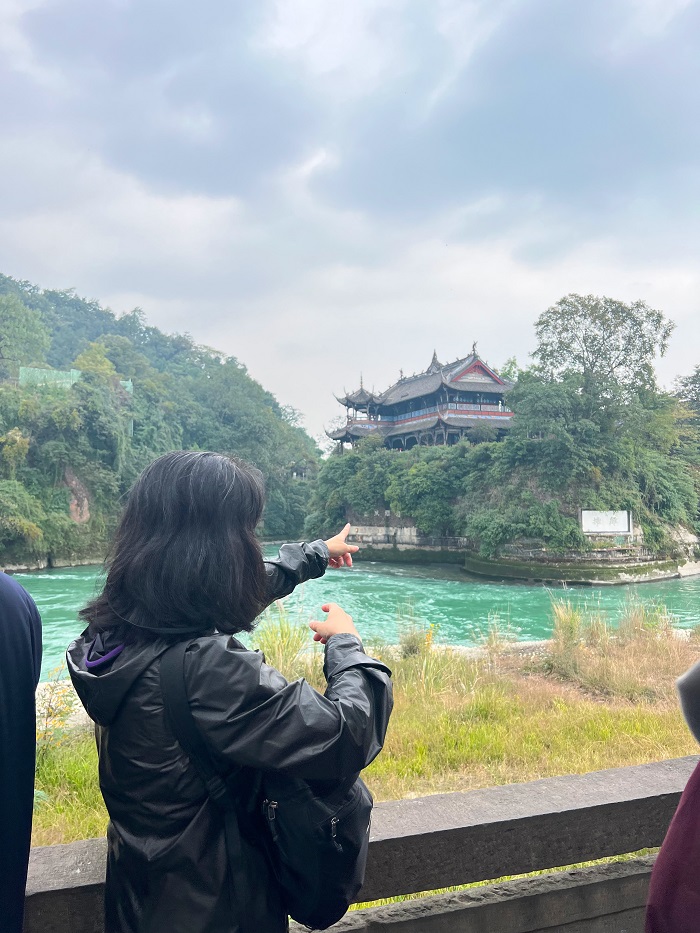 A CET Beijing student pointing towards a building by the interior river of the Dujiangyan Irrigation System in Chengdu