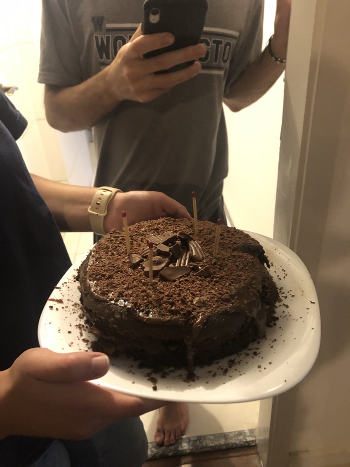 Someone holding a chocolate cake on a plate with four matches sticking out as candles