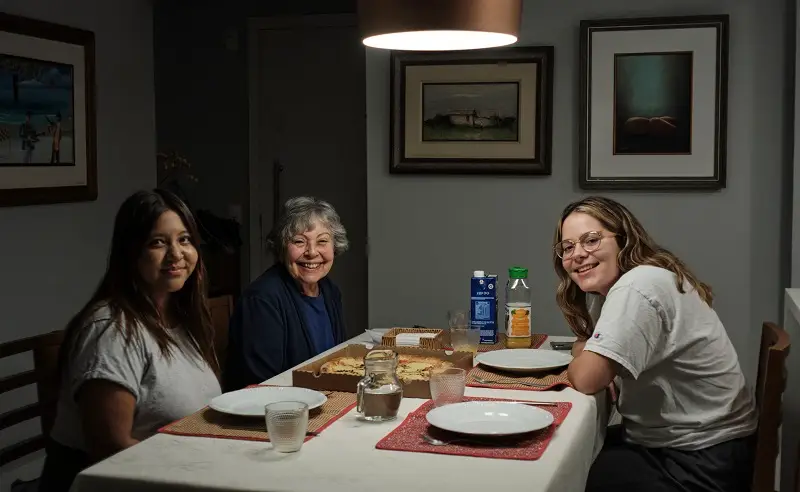 A CET Brazil Social Justice student sitting across a girl and her grandma at a table with pizza