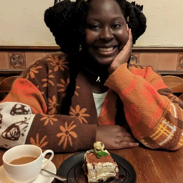 A CET Japan student smiling with one hand on her cheek while sitting in front of a dessert and cup of coffee