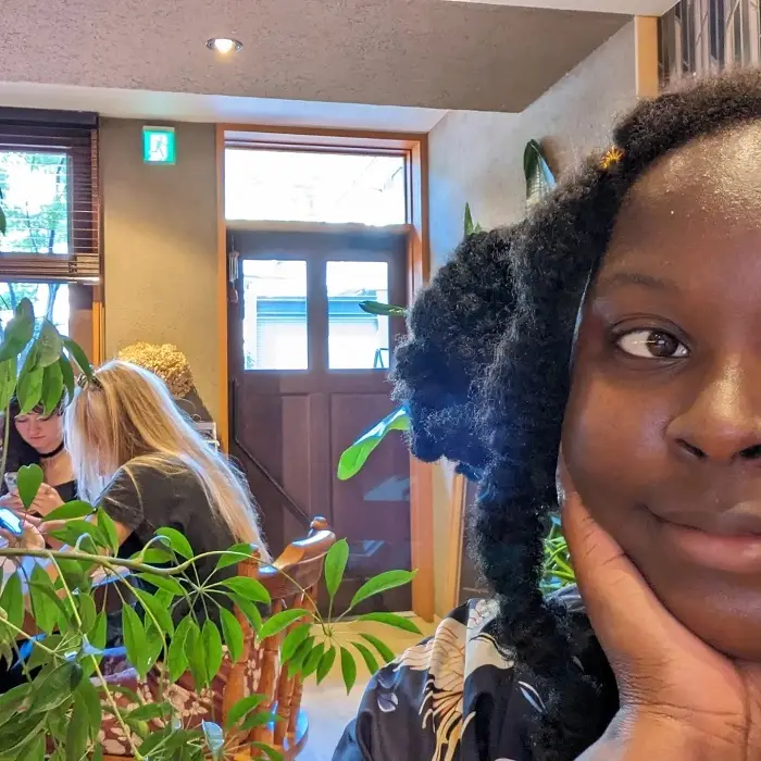 Half of the face of a CET Japan student smiling with one hand on her cheek while indoors