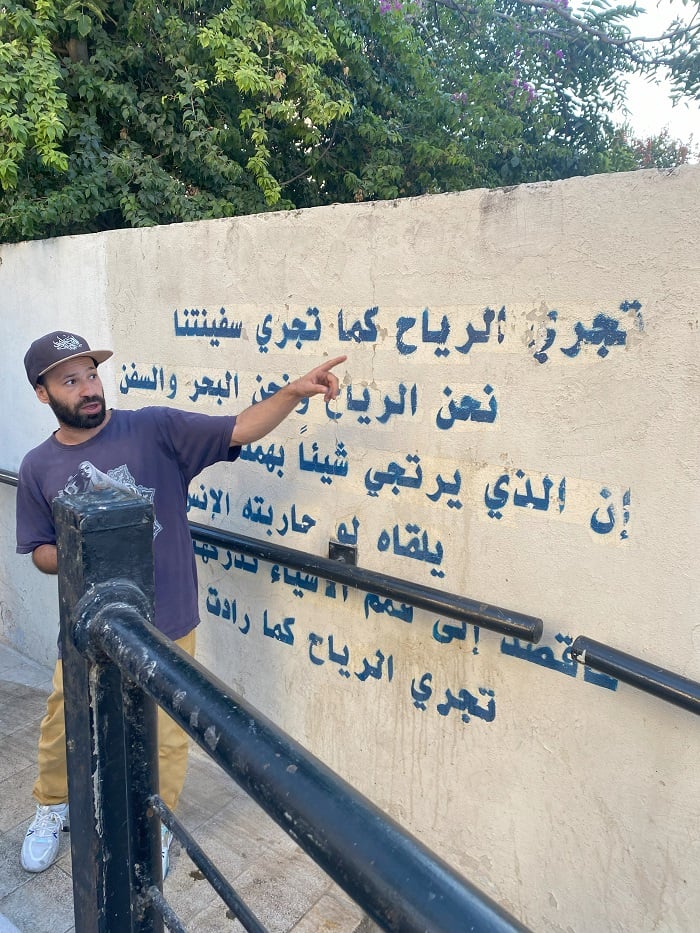A man named Alaeddin Rahmeh, founder of Underground Amman, pointing to Arabic words on a wall