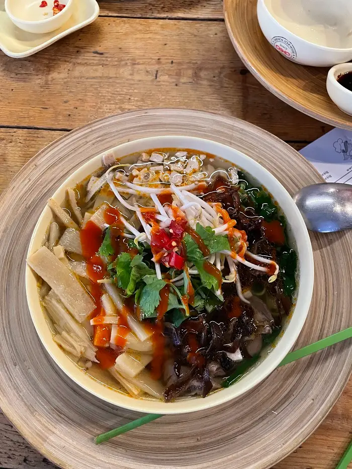 A bowl of Pho including bean sprouts, cilantro, hot sauce, mushrooms and more
