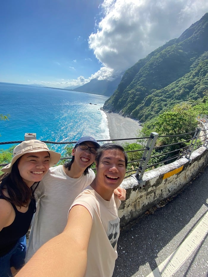 A CET Taiwan local roommate posing with two other people on the street overlooking clear blue waters and a part of a beach