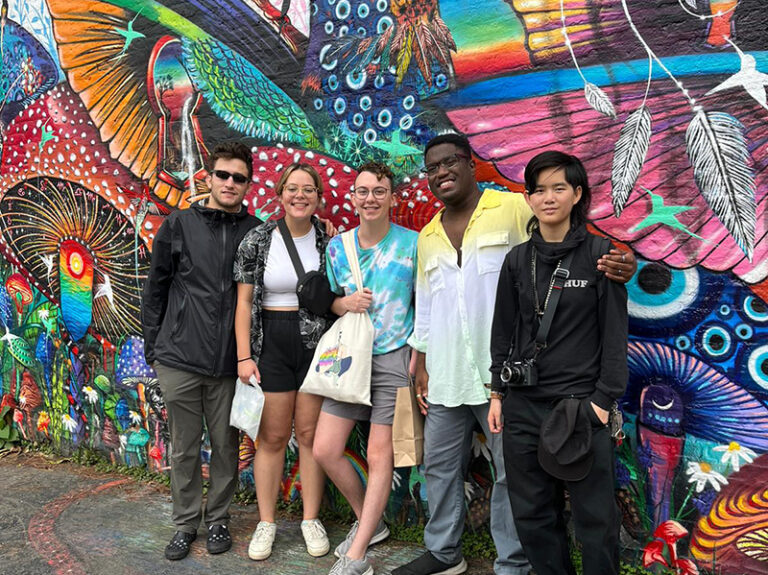 group of students smiling in front of colorful street art