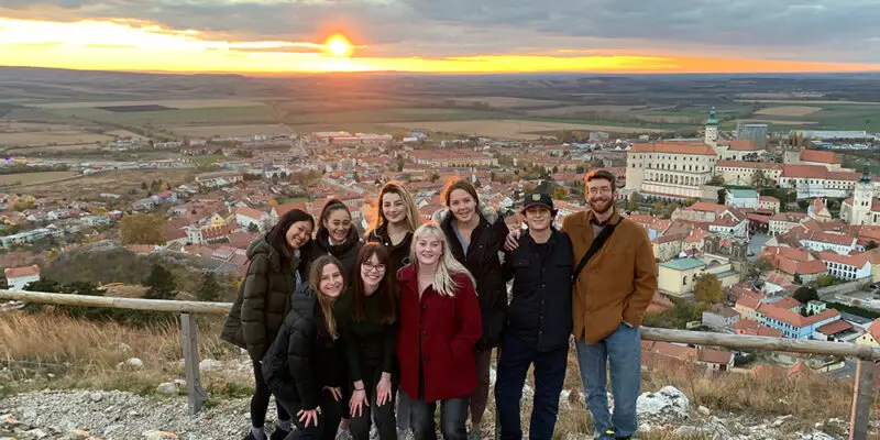students smiling in front of sunset over city