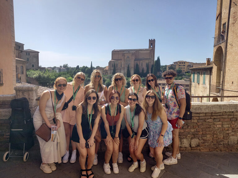 group of students smiling at camera with view of Italy behind