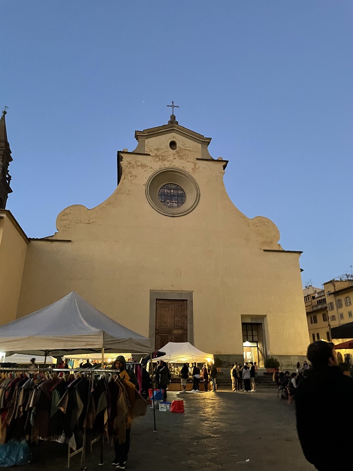 Tents selling clothing, jewelry, and other items outdoors in Piazza Santo Spirito in the late evening
