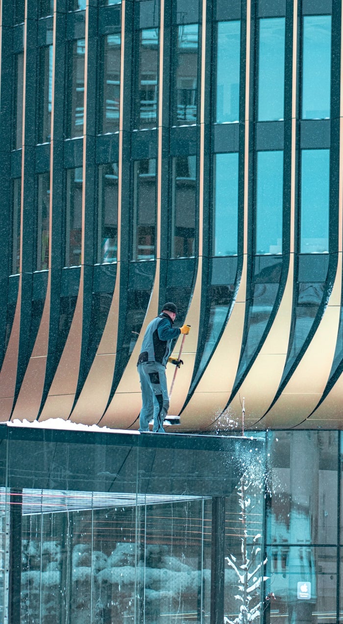 A worker pushing off snow to the floor from the top of a building in Prague