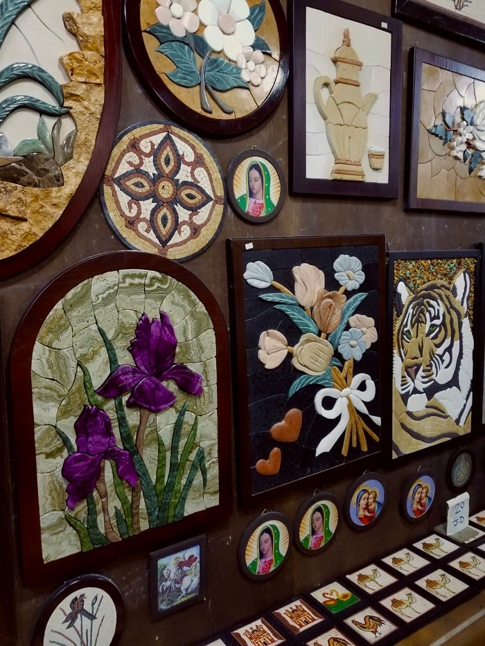 A variety of mosaic art on a wall of a different pieces including tiger, flowers, and more in Madaba