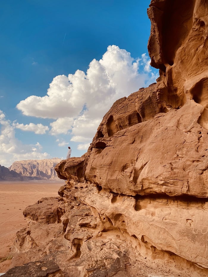 A man standing peacefully on top of this cliff, overlooking the beauty that is Wadi Rum in Jordan