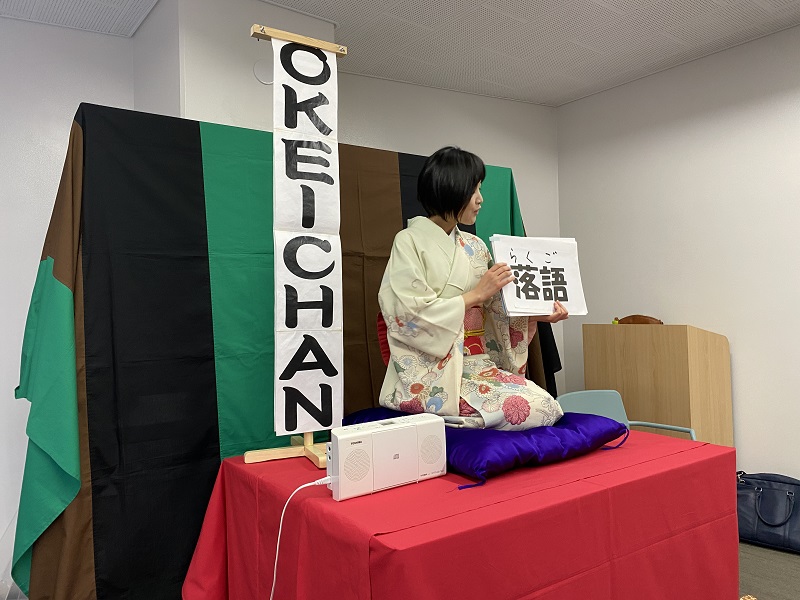 A Rakugo teacher holding papers with Japanese characters while wearing a kimono and sitting on a table 