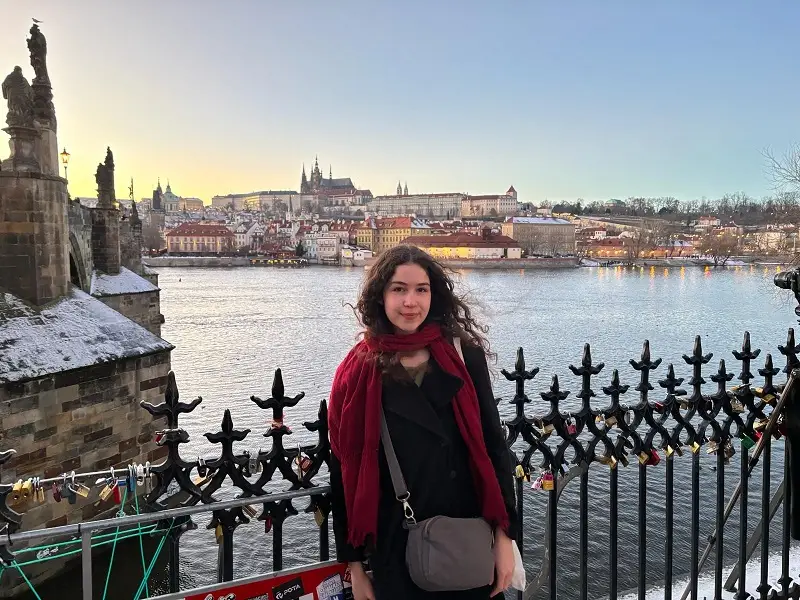 A CET Prague student standing by Charles Bridge with a view of the city in the background by water