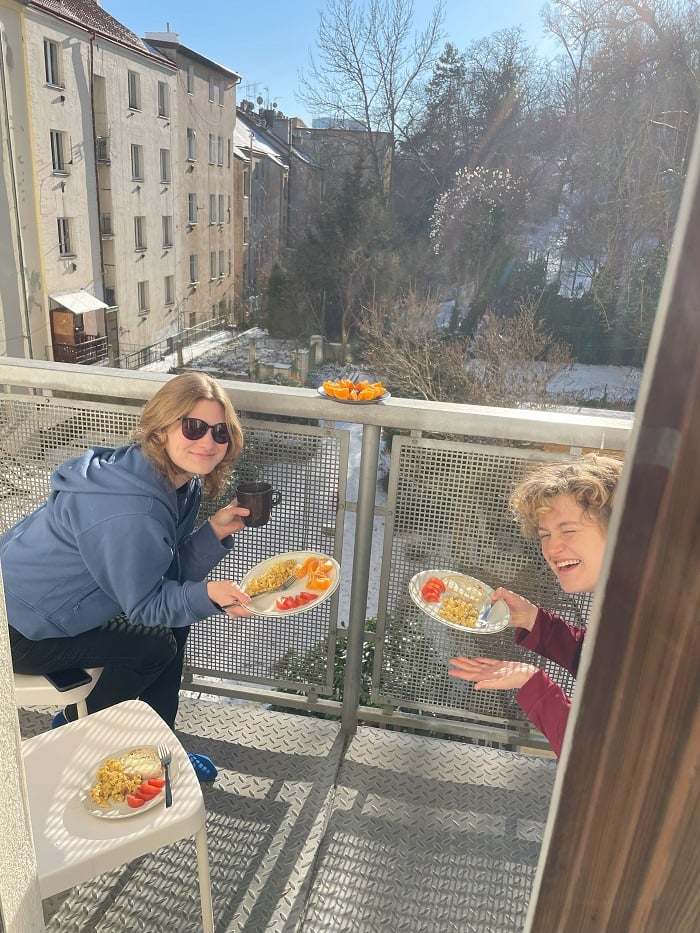 Two CET Prague students sitting on chairs with plates of breakfast and fruits outside on their apartment patio