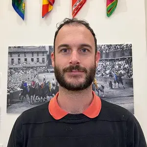 A shoulders and up photo of Davide wearing a black sweater and an orange collar.