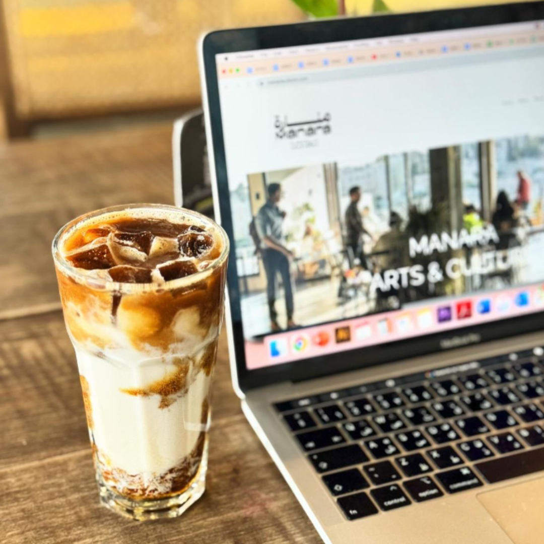 A cup of iced almond milk latte next to a laptop opened to a website on a table