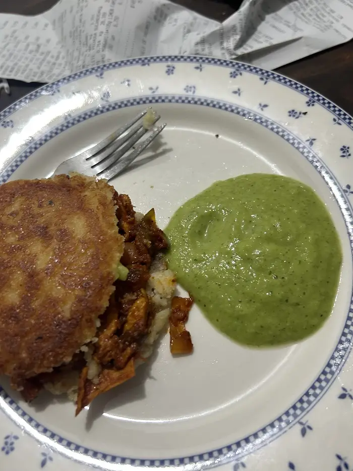 An arepa with some sauce on the side and a fork