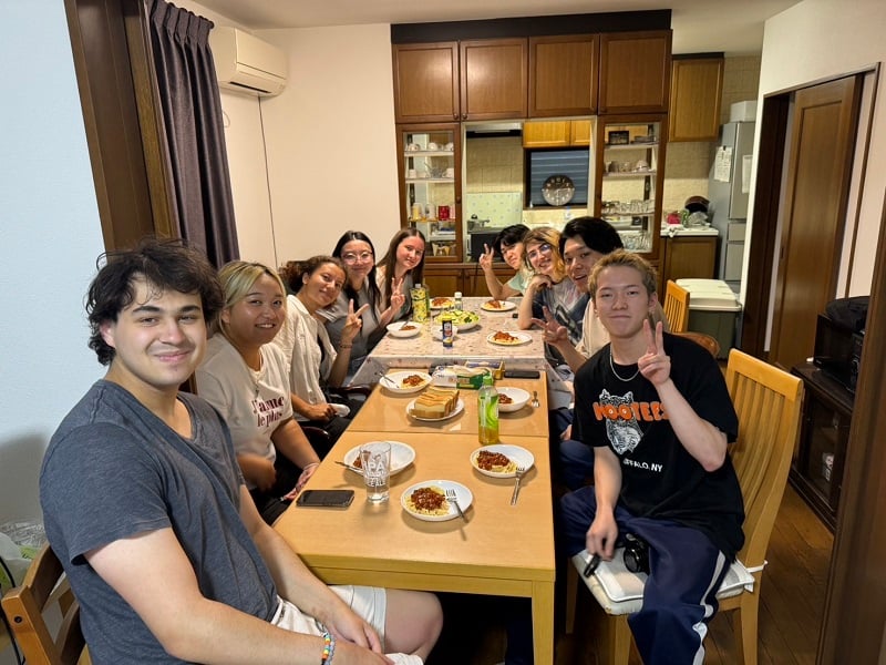 A large group of CET Japan students and local roommates eating together around a table with plates of pasta