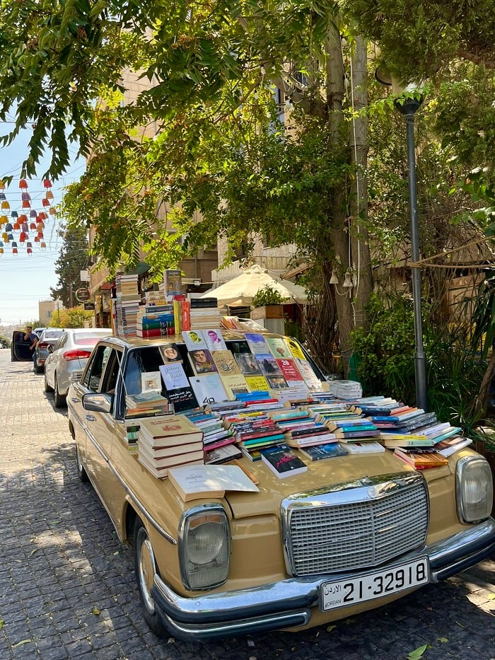 A car under a tree with books all over it with rainbow lanterns in the background in Amman, Jordan