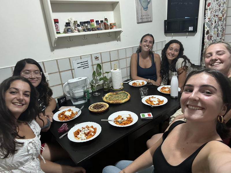 A group of CET Siena students and local roommates sitting around a table with pasta in an apartment