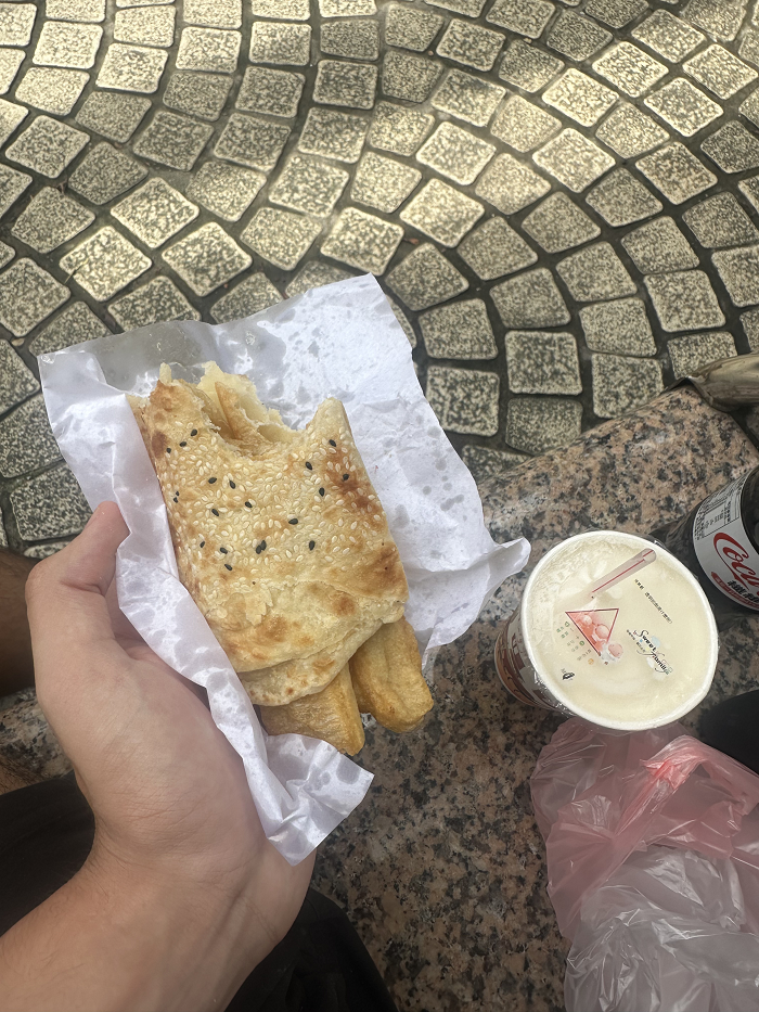 A boba drink on the side with a hand holding an eaten shāobǐng 