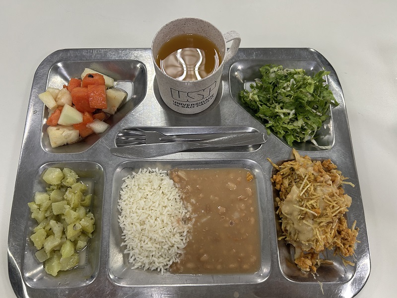 A standard lunch tray with vegetables, rice, beans, greens, and a mug with the Universidade de São Paulo inscription 