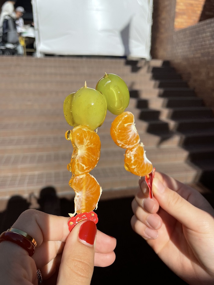 Two hands holding a tiny stick of fruits glazed in sugar candy called tanghulu at the Kishibe Festival