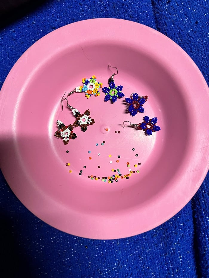 Three pairs of little beaded earrings placed alongside small beads within a bowl