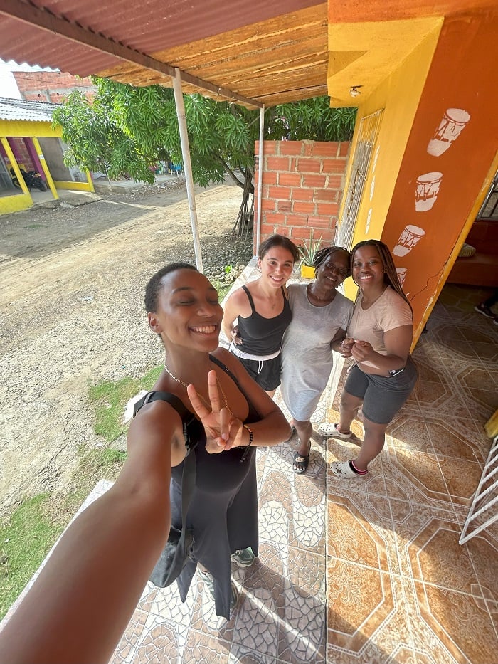 A CET Colombia student holding up a peace sign and smiling with her local host mom and local roommates at a home in San Basilio de Palenque