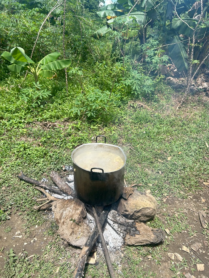 A large pot of boiling soup over a small fire on the ground 