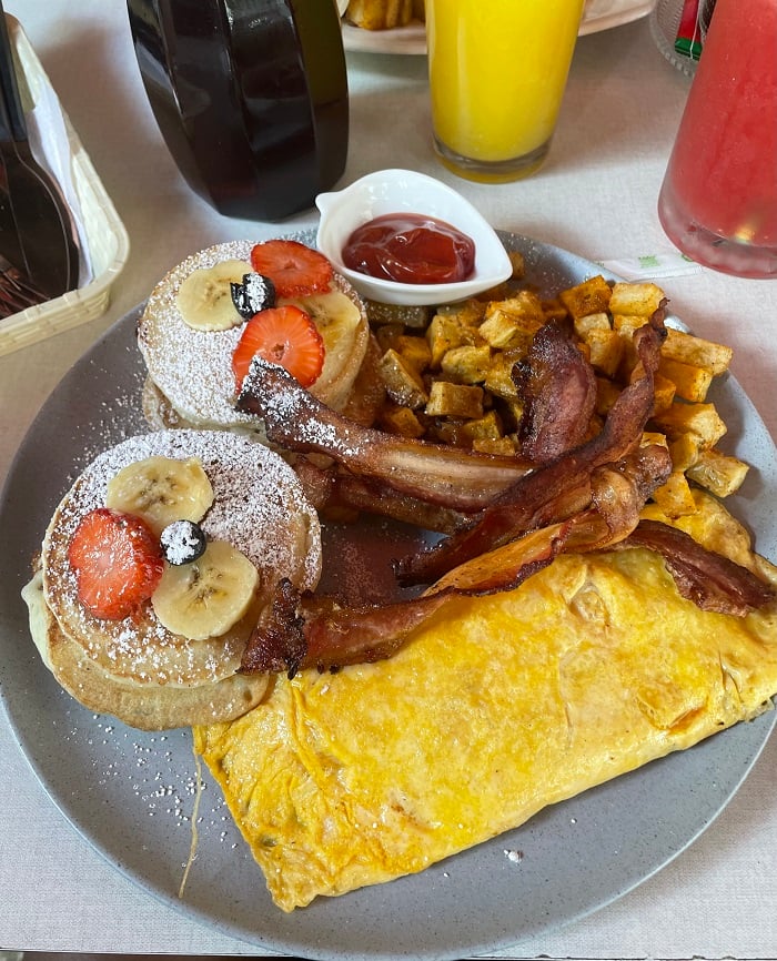 Bacon, pancakes, small potatoes, and an omelet on a plate from The Sweet Georgia Café 