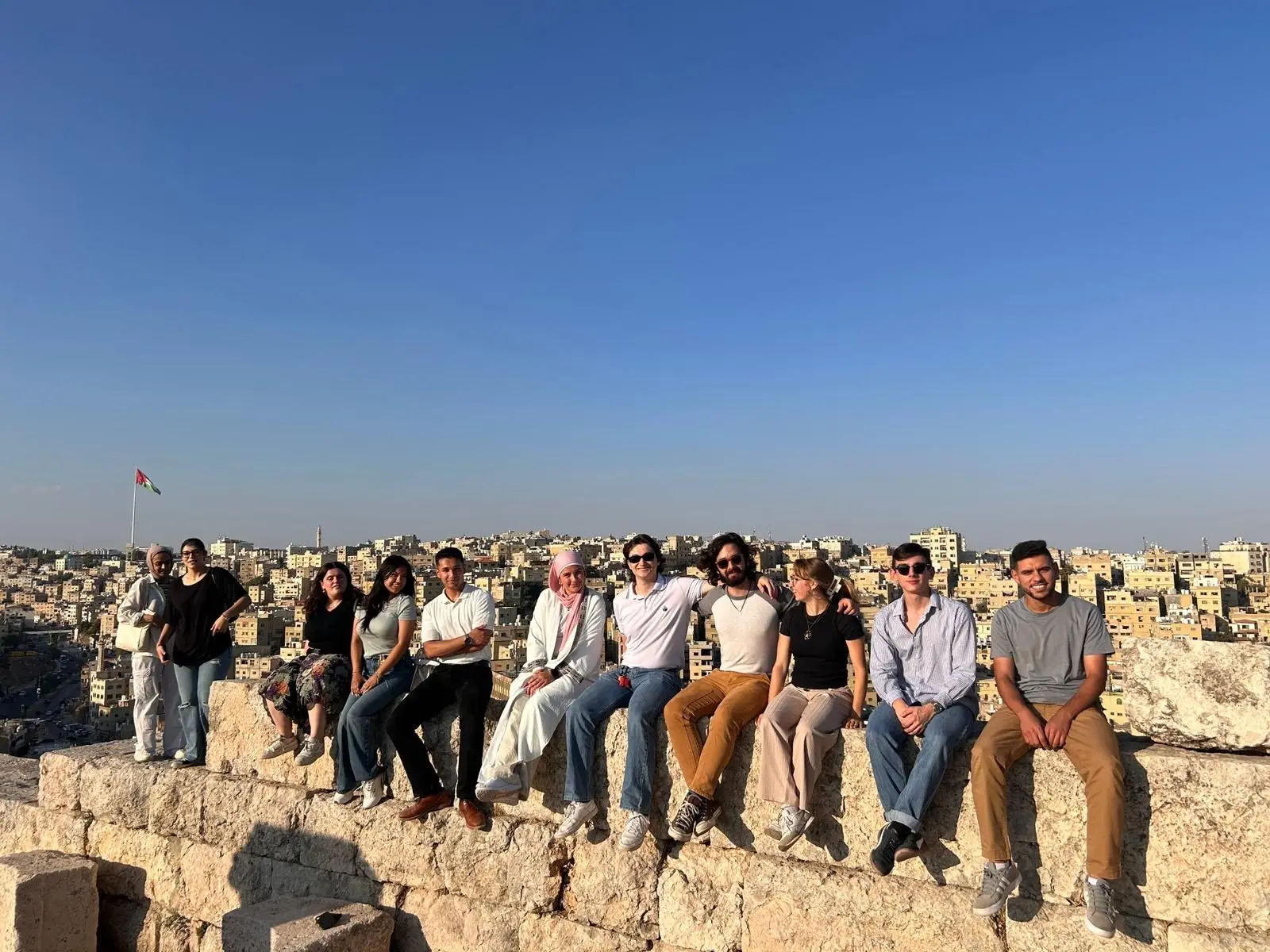 A group of CET Jordan students and local Jordanian neighbors sitting along a wall at the Citadel in Jordan