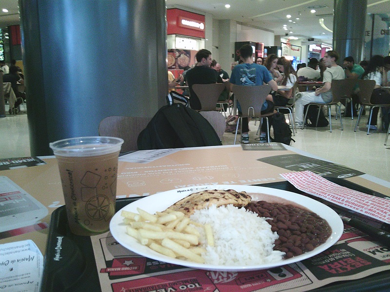 A plate of prato feito, including beans, fries, rice, on a tray with a drink