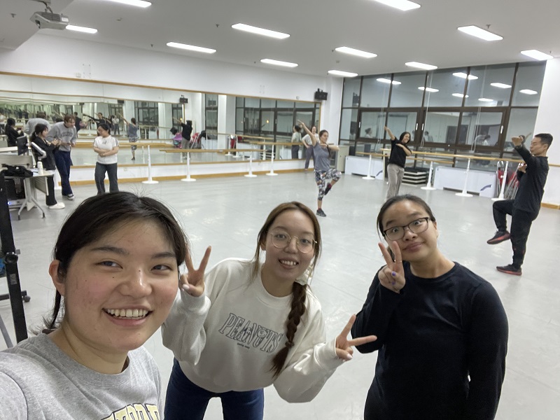Three students posing in a room for a washu class with a large mirror and other students practicing