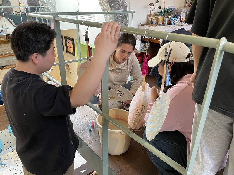 People dipping fans inside a bucket of paint and hanging them to dry