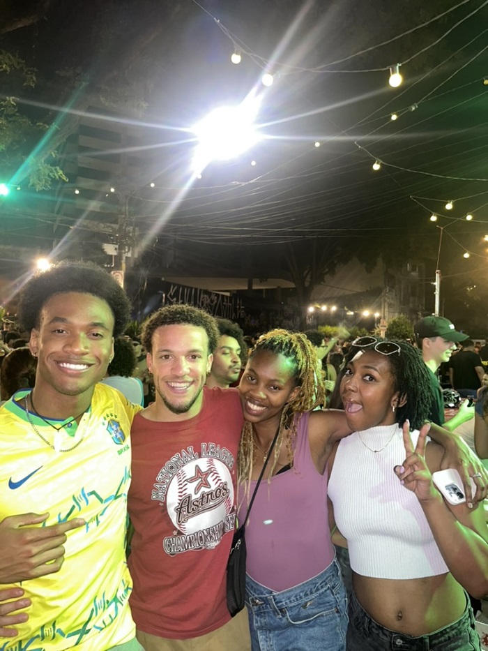 Four students standing outside and smiling while in the middle of a huge crowd in Pinheiros at night