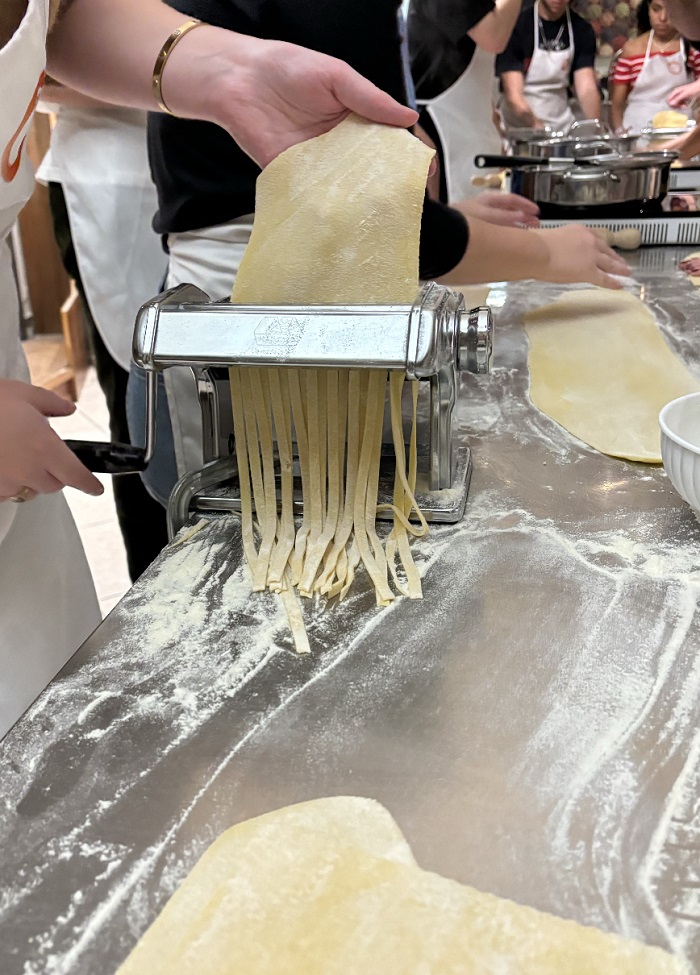 A flat piece of dough being rolled out through a machine to make fresh pasta noodles
