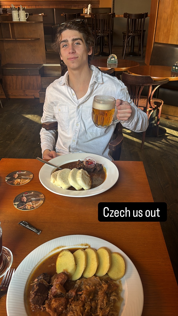 A boy holding up a pitcher of beer with traditional Czech food in front of him at a restaurant