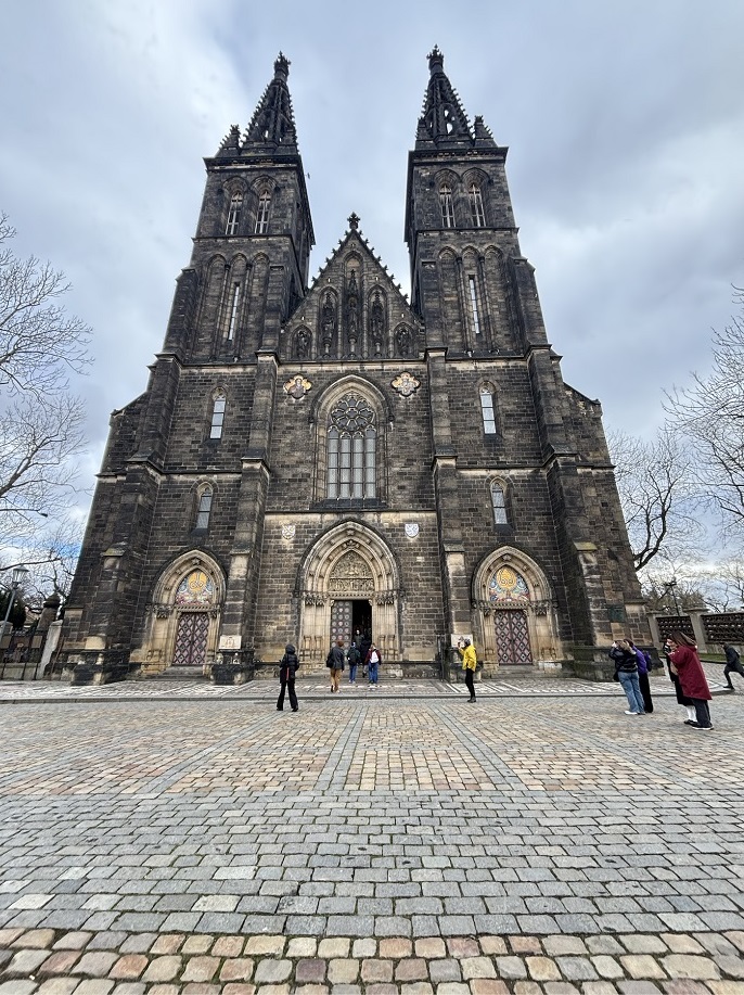 A couple of people standing outside of the Vysehrad Church on a gloomy day