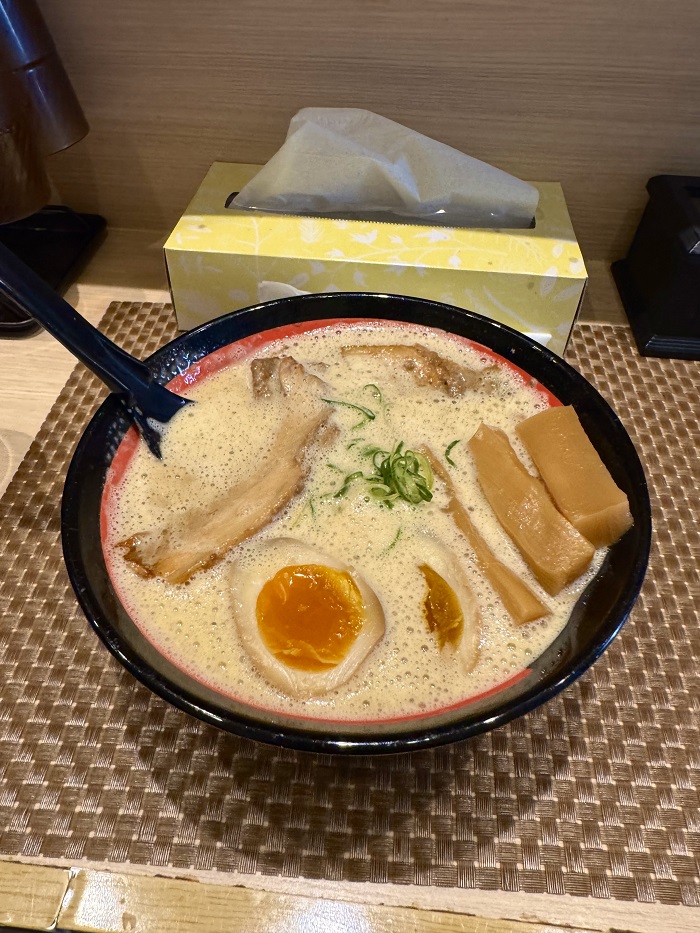 A close-up of a creamy ramen bowl topped with a thick slab of pork belly, green onions, a marinated egg, and bamboo shoots