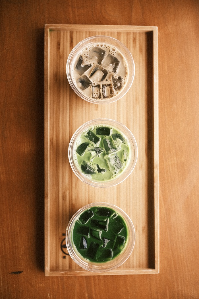Three drinks of matcha lined up on a wooden tray