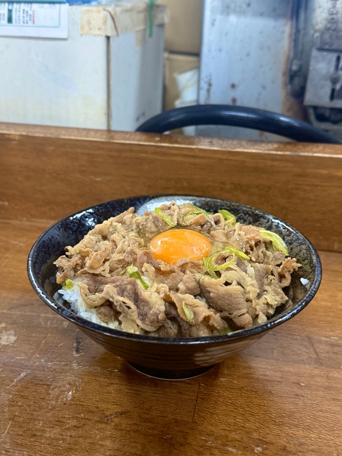 A rice bowl with marinated beef, onions, and egg over rice