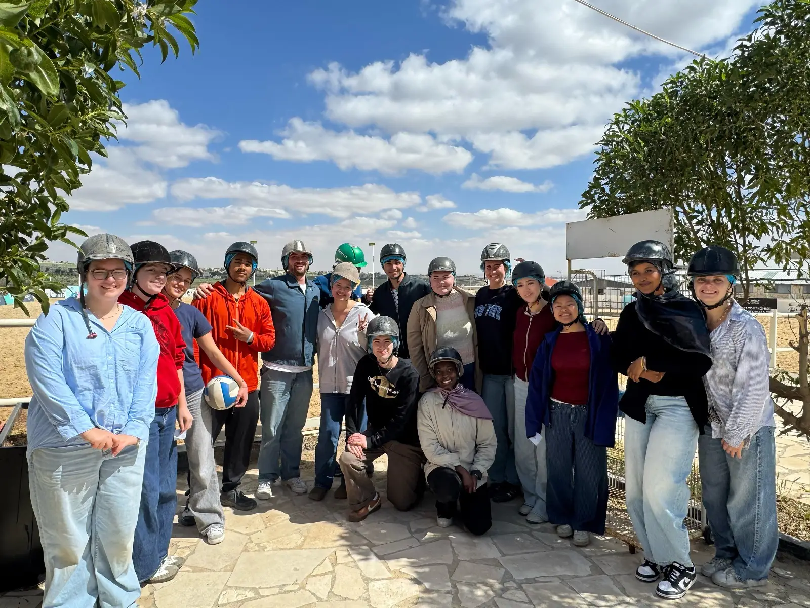 A large group of CET Jordan students wearing riding helmets while smiling outdoors on a partly cloudy day
