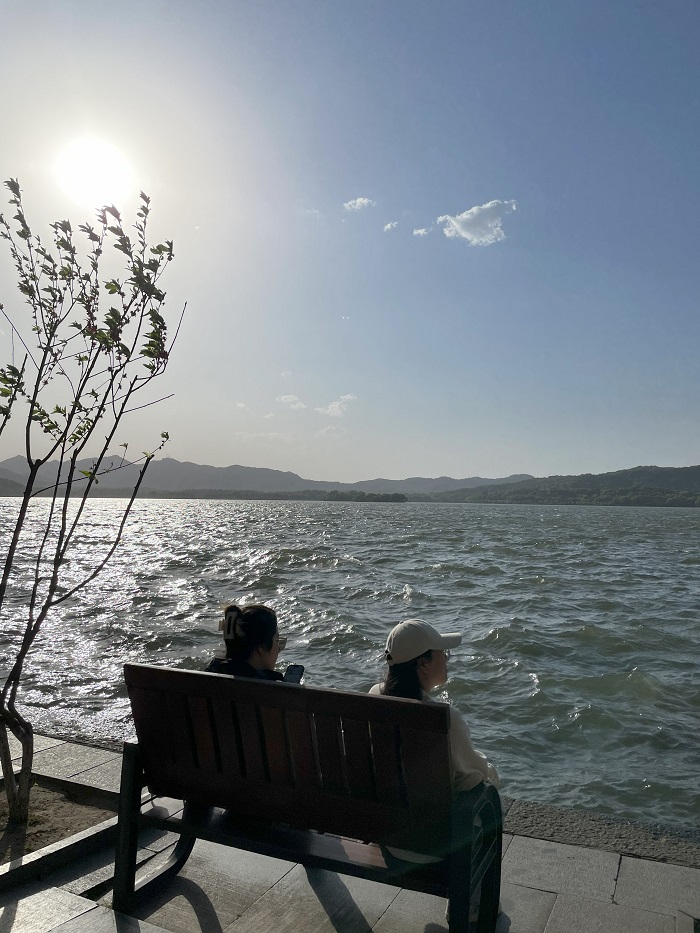 Two people sitting on a bench by the Hangzhou West Lake on a sunny day